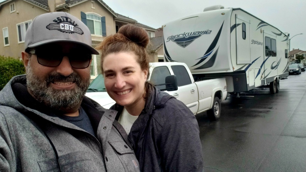 Couple standing in front of a Shockwave Fifth wheel toy hauler trailer and white truck